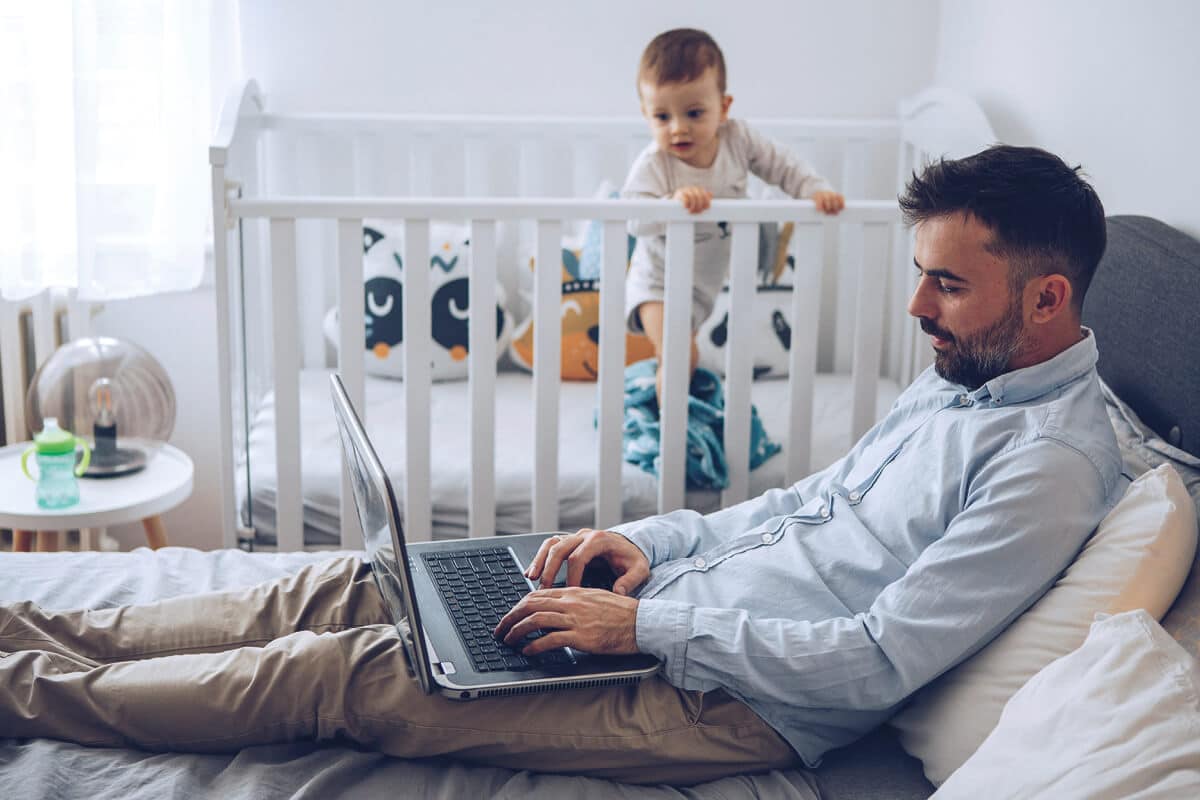 Vater arbeitet am Laptop neben seinem Kind